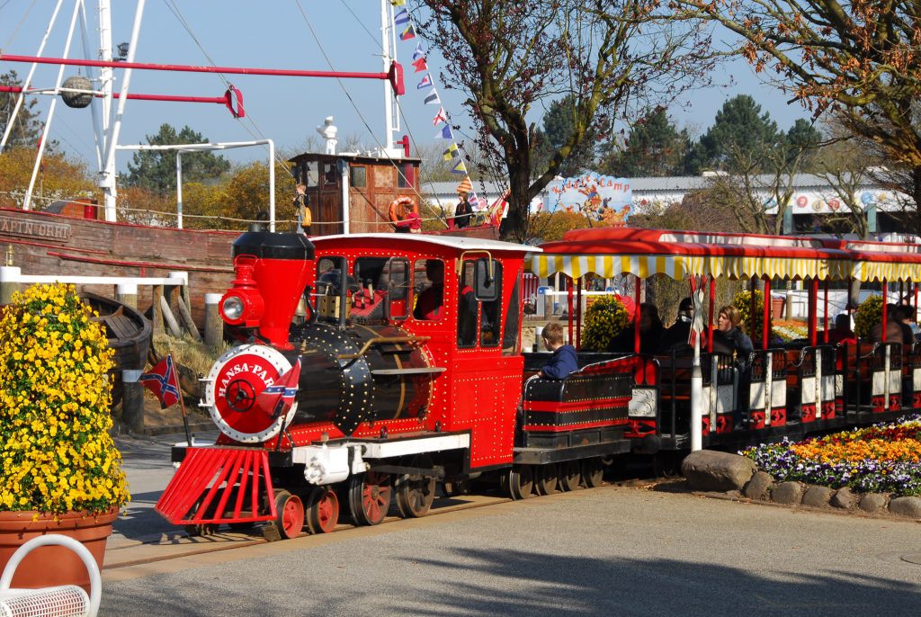 Rote Parkbahn im Hansa-Park in Sierksdorf mit Fahrgästen und Hansekogge im Hintergrund